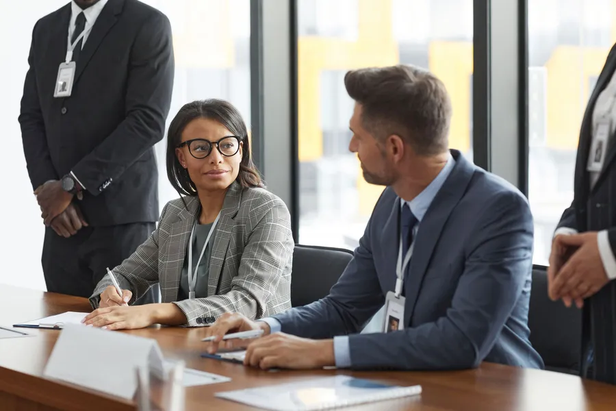 Two colleagues in suits discussing a contract across a meeting table