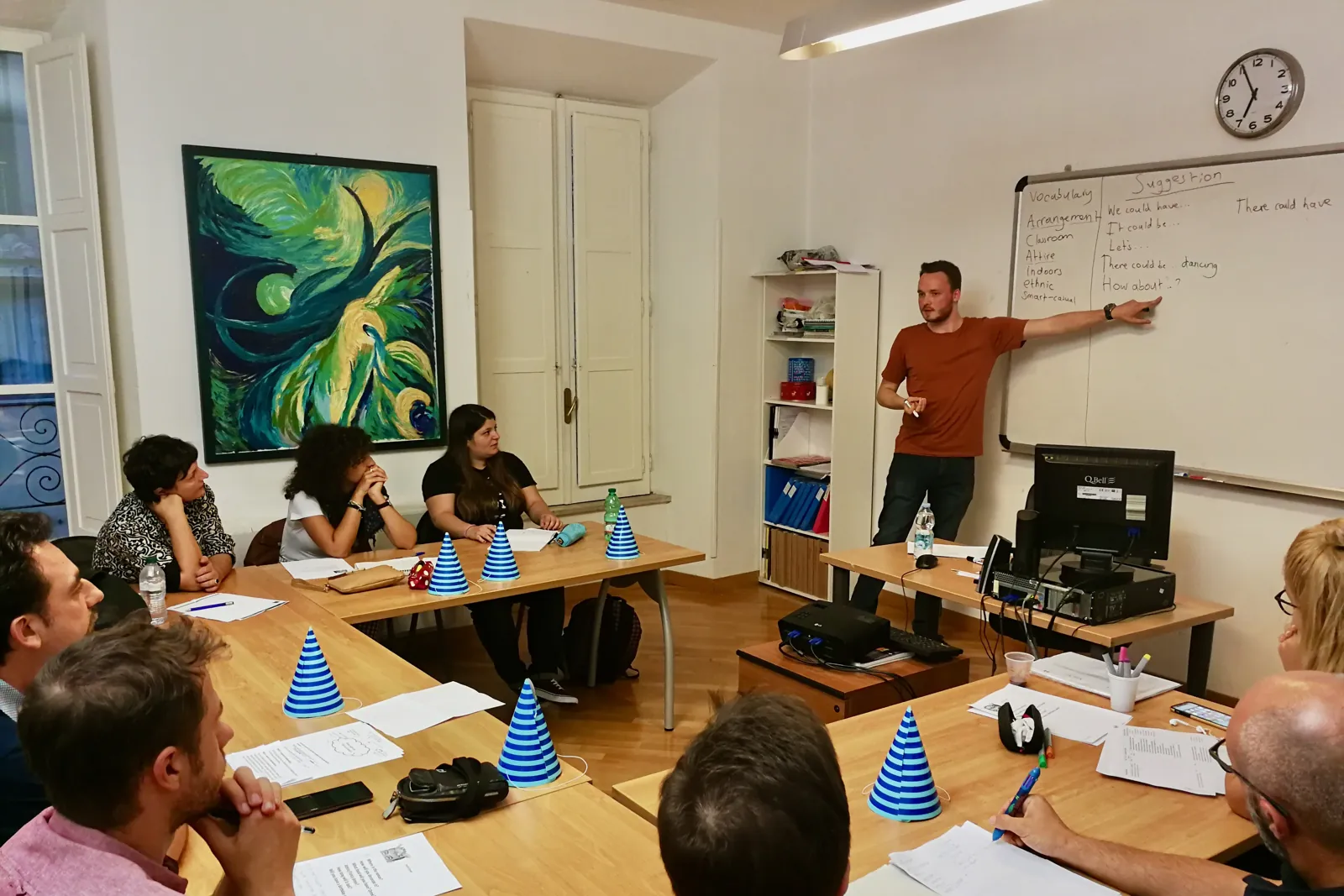 Anthony leading a group lesson, pointing at phrases on a whiteboard while students around a table listen